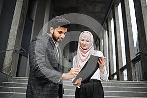 Woman in hijab holding clipboard while man signing contract