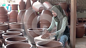 woman in hijab sitting processing clay into pottery in studio