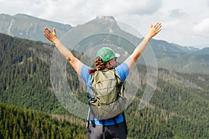 Woman hiker with backpack open arms at mountain peak. Travel and active lifestyle concept. 30s girl enjoying valley view