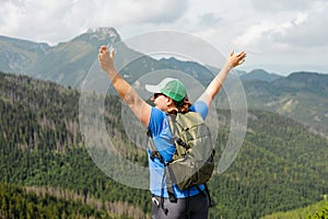 Woman hiker with backpack open arms at mountain peak. Travel and active lifestyle concept. 30s girl enjoying valley view