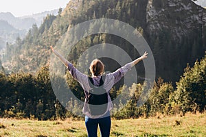 Woman hiker with backpack open arms at mountain peak. Travel and active lifestyle concept. 30s girl enjoying valley view