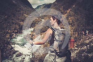 Woman hiker with backpack standing on the edge of the cliff with epic wild mountain river view.