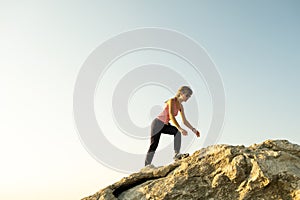 Woman hiker climbing steep big rock on a sunny day. Young female climber overcomes difficult climbing route. Active recreation in