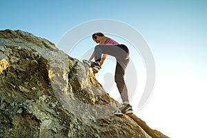 Woman hiker climbing steep big rock on a sunny day. Young female climber overcomes difficult climbing route. Active recreation in