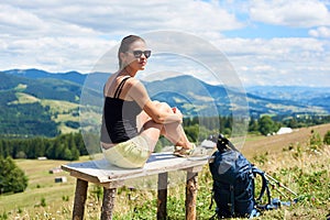 Woman hiker hiking on grassy hill, wearing backpack, using trekking sticks in the mountains