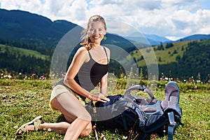 Woman hiker hiking on grassy hill, wearing backpack, using trekking sticks in the mountains