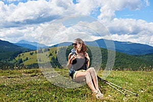 Woman hiker hiking on grassy hill, wearing backpack, using trekking sticks in the mountains