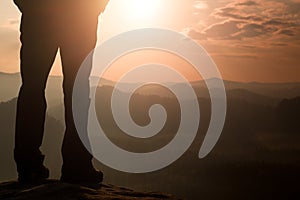 Woman hiker legs in tourist boots stand on mountain rocky peak. Sunny day