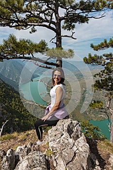 Woman hiker at mountain viewpoint resting on a rock with lake and canyon in the background