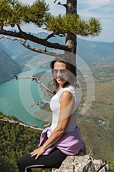 Woman hiker at mountain viewpoint resting on a rock with lake and canyon in the background