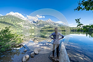 Woman hiker poses looking out over Bradley Lake after a hike, in Grand Teton National Park