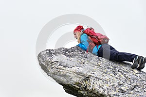 Woman hiker with red backpack sits at the edge of a cliff and looks down amazed and scared, isolated by fog. Hiking in Slovakia
