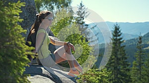 Woman hiker sitting alone on rocky mountain enjoying view of nature on wilderness trail. Active way of life concept