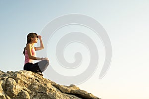 Woman hiker sitting on a steep big rock enjoying warm summer day. Young female climber resting during sports activity in nature.