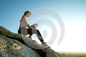 Woman hiker sitting on a steep big rock enjoying warm summer day. Young female climber resting during sports activity in nature.