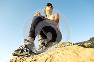 Woman hiker sitting on a steep big rock enjoying warm summer day. Young female climber resting during sports activity in nature.