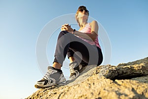 Woman hiker sitting on a steep big rock enjoying warm summer day. Young female climber resting during sports activity in nature.