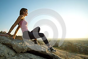 Woman hiker sitting on a steep big rock enjoying warm summer day. Young female climber resting during sports activity in nature.