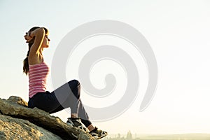 Woman hiker sitting on a steep big rock enjoying warm summer day. Young female climber resting during sports activity in nature.