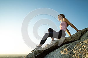 Woman hiker sitting on a steep big rock enjoying warm summer day. Young female climber resting during sports activity in nature.