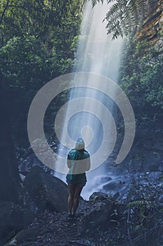 Woman hiker standing below a waterfall after rain