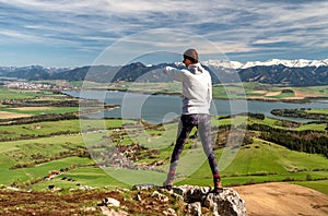 Woman hiker standing on top of the hill and looking on beautiful nature with lake and snowy mountains in region Liptov at Slovakia