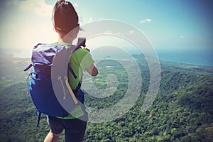 Woman hiker taking photo with cellphone hiking on mountain peak