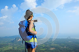 Woman hiker taking photo with cellphone hiking on mountain peak