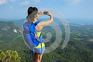 Woman hiker taking photo with cellphone hiking on mountain peak