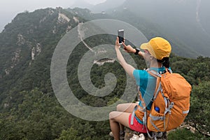 Woman hiker taking photo with smart phone on top of great wall