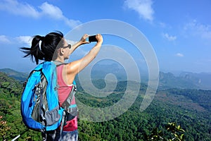 Woman hiker taking photos with cellphone at mountain peak