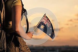 Woman hiker on the top of mountain in shorts and a t-shirt with a backpack and flag of Australia on a sunset sky background.
