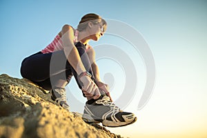 Woman hiker tying shoe laces of her sport boots while climbing steep big rock on a sunny day. Young female climber overcomes