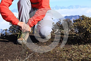 Woman hiker tying shoelace of hiking boots on mountain peak