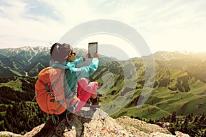Woman hiker use digital tablet taking photo on mountain peak cliff