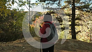 A woman hiker walks to the edge of a slope in an autumn mountain forest.