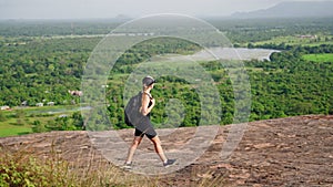 Woman hikes rocky terrain, expansive views atop Pidurangala Rock. Adventure seeker with backpack enjoys tranquil nature