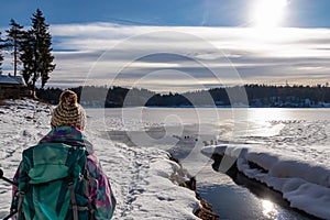 Woman with hiking backpack watching ducks on the frozen lake Forstsee, Techelsberg, Carinthia (Kaernten), Austria, Europe.