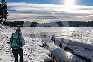 Woman with hiking backpack watching ducks on the frozen lake Forstsee, Techelsberg, Carinthia (Kaernten), Austria, Europe.