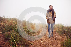 Woman, hiking and field with trekking sticks, winter and support for fog trail in mountain. Athlete, backpack and