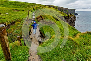 Woman hiking on a rainy day from Doolin to the Cliffs of Moher along the spectacular coastal route walk