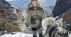 Woman, hiking and snow in winter, dog and backpacker on mountain, animal and holiday. Vacation, pet and Alaskan Malamute