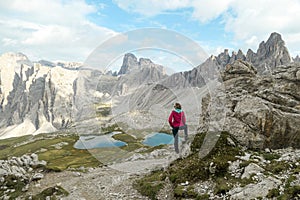 Woman hiking with the view on small, navy blue lakes at the bottom of the valley in Italian Alps.