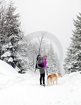 Happy woman walking in winter forest with dog