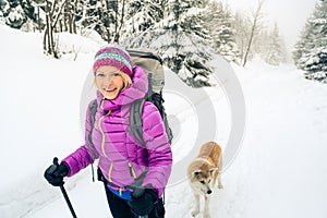 Happy woman walking in winter forest with dog