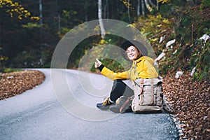 Woman hitchhiker by the roadside among autumn forest