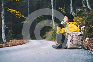 Woman hitchhiker by the roadside among autumn forest