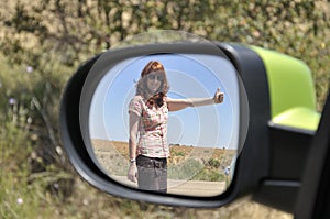 Woman hitchhiking reflected in the rearview mirror