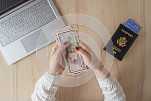 Woman hold banknote 50 U.S. dollars in hand and count it. American passport with boarding pass and laptop on the table.