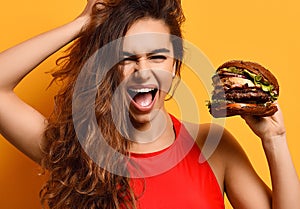 Woman hold big barbecue burger sandwich with hungry mouth happy screaming laughing on yellow background